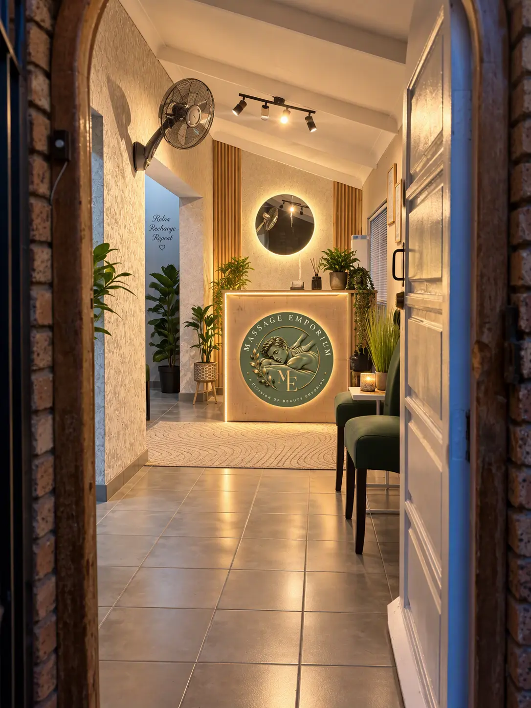 Massage Emporium reception desk with the glowing logo, plants and green chairs